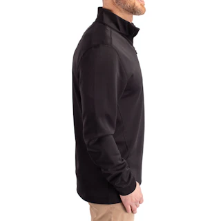 A man standing in profile and wearing a black quarter zip pullover with khaki pants.