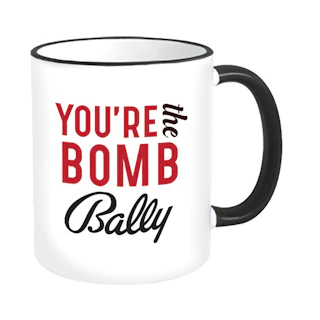 A white ceramic mug with a black handle and printed with You're the Bomb Bally in red and black.
