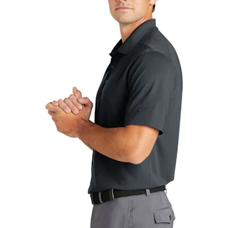 A man standing in profile wearing a dark gray Nike polo shirt with his hands clasped together.