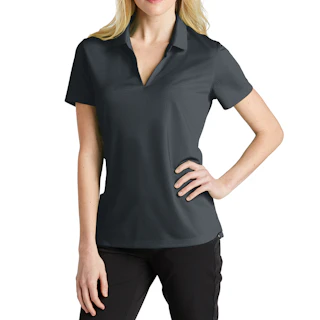 A woman standing and wearing a dark gray Nike polo shirt with her right hand on her hip and black pants.