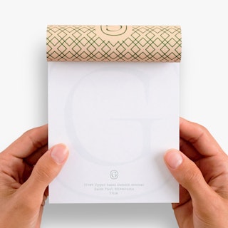Two hands holding a branded notepad with Grandier Hotel info and one page flipped over the top.