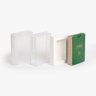 Four playing card boxes lined up in a row, including a green one, white white and two clear ones.