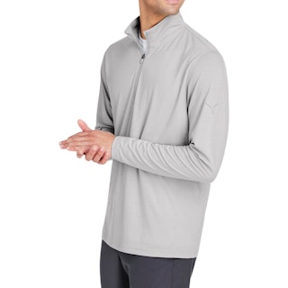 A man standing to the side wearing a light gray Puma quarter zip pullover with his hands clasped together.