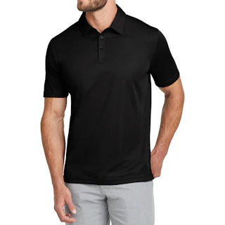 A man wearing a solid black polo business shirt with light gray pants and his right hand in the pocket.