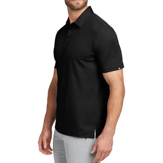 A man standing to the side wearing a black company polo with light gray pants.