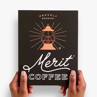 Two hands holding a custom metal sign printed with Proudly Serving Merit Coffee and a lantern graphic.