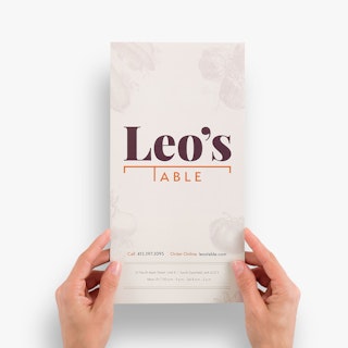 Two hands holding a restaurant menu printed with Leo's Table on the front in maroon and orange.