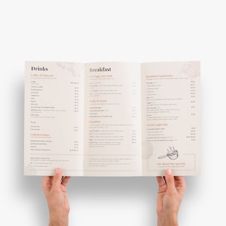 Two hands holding open a custom menu printed with three panels and listings for drinks and breakfast.
