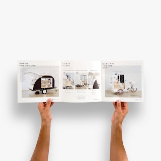 Two hands holding open a custom tri-fold brochure printed with images of mobile retail carts.
