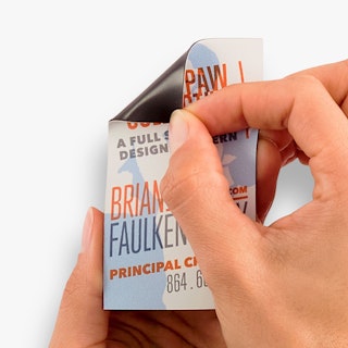 Two hands holding a business card magnet and folding back the top left corner.