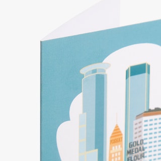 The top corner of a custom card printed with a blue and orange design on buildings in downtown Minneapolis.