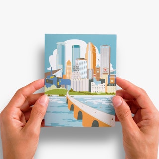 Two hands holding a custom card printed with a graphic of Minneapolis in blue, green and orange.
