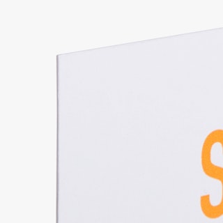 The top left corner of a cardstock sign printed with a white background and an orange letter.