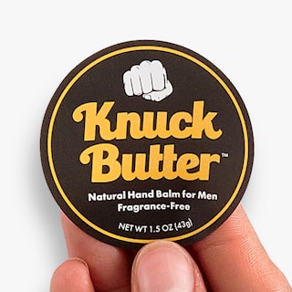 A hand holding a round label custom printed with Knuck Butter in yellow, white and black.