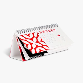 A desk calendar printed with a red, white and black design and black wire coil binding.