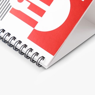 The corner of a desk calendar with a black wire coil binding and a red and white cover.