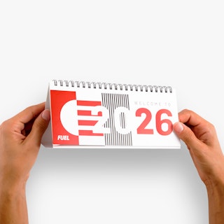 Two hands holding a desk calendar printed with Welcome to 2026 in red, black and white on the cover.