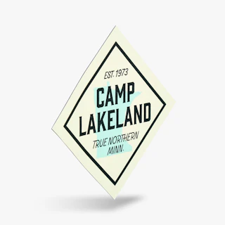 A die-cut magnet printed with Est. 1973, Camp Lakeland and True Northern Minn. in black, cream and blue.