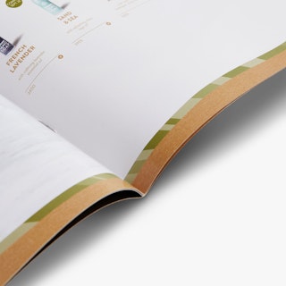 The spine of a direct mail catalog laying open and printed with a green and tan border and soap products.