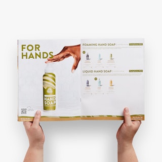 Two hands holding open a direct mail catalog printed with hand soap images and product details.