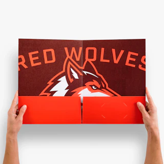Two hands holding open a pocket folder printed with Red Wolves and a wolf graphic in orange and red.