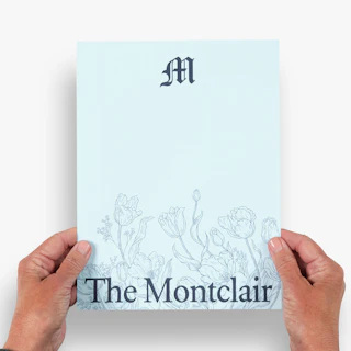Two hands holding an assisted living marketing sheet printed with The Montclair and a floral graphic.