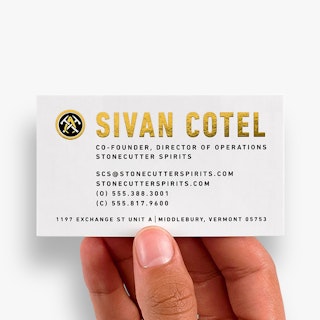 A hand holding a custom business card printed with Sivan Cotel in gold foil with contact info in black.