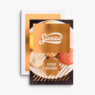 Two flat cards overlapping each other and printed with rose gold foil and Sanaa Artisan Macarons on the front.