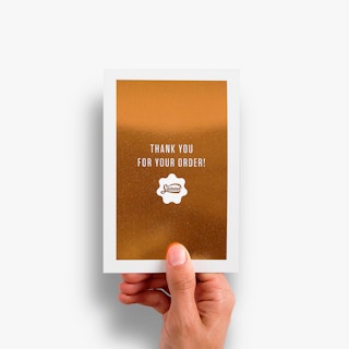 A hand holding a flat card printed with a flood of rose gold foil and Thank You For Your Order in white.