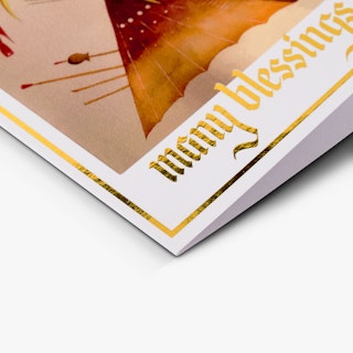 The bottom corner of a custom greeting card printed with Many Blessings in gold foil and indigenous artwork.
