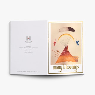 A greeting card laying flat open with Many Blessings and accents in gold foil, plus indigenous artwork.