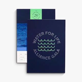 Two foil invitations overlapping each other with a blue water design, gala details and blue-green foil.