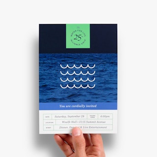 A hand holding an event invitation printed with date and location details and a water-themed design.