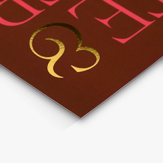 The corner of a custom wedding invite printed with a maroon background and foil in red and gold foil.
