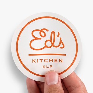 A hand holding a custom food label printed with a white and red design and Ed's Kitchen SLP.
