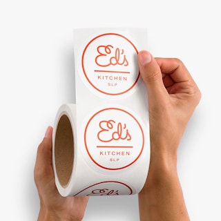 Two hands unrolling a roll of food label printed with Ed's Kitchen SLP in white and red.