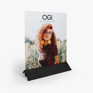 A free-standing sign printed with OGI Eyewear and a woman wearing glasses in a black holder.
