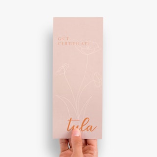 A hand holding a gift certificate printed with Tula and a floral design in pink, white and orange.