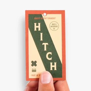 A hand holding an apparel hang tag printed with a Hitch design in green and orange.
