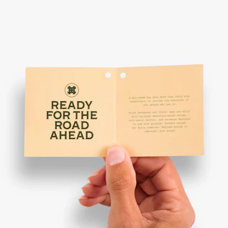 A hand holding open a custom printed hang tag with Ready for the Road Ahead on the left.