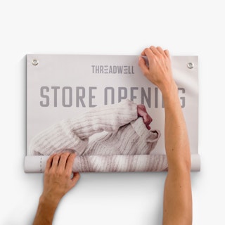 Two hands unrolling a hanging banner printed with Threadwell Store Opening in cream and gray.