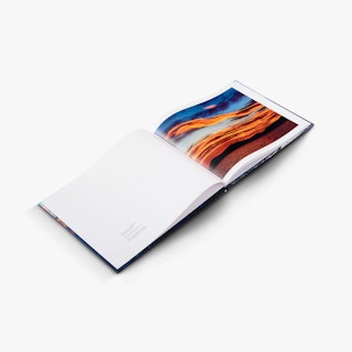 A hardcover book laying open to a sunset image in blue, orange, red and brown.