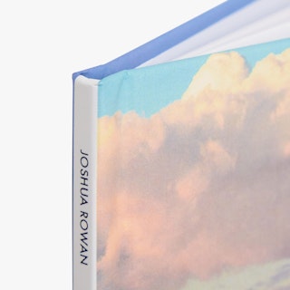 The top corner of a photography book printed with a cloud design on the cover and Joshua Rowan on the spine.