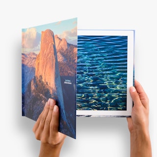 Two hands holding open a hardcover book printed with landscape and nature photography.