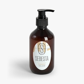 A brown bottle of lotion with a custom label printed in an oval shape and Sebesta Apothecary.