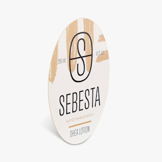 A lotion bottle label printed with an oval shape, black and tan design and Sebesta Apothecary.