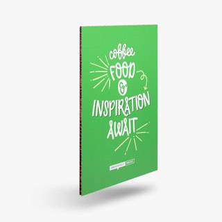 A honeycomb cardboard sign printed with a green background and Coffee, Food & Inspiration Await in white.