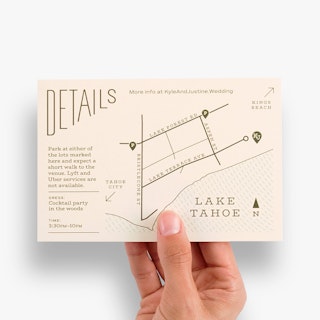 A hand holding a wedding map card printed with venue details and directions in dark green.