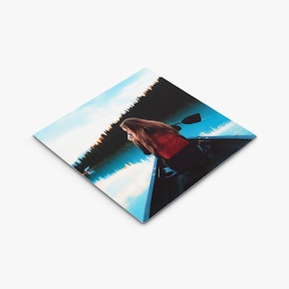 A custom metal print with an image of a woman wearing a red backpack paddling a canoe on a lake.