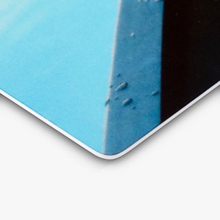 The rounded corner of a custom metal print with a few water droplets on it and a blue and black design.